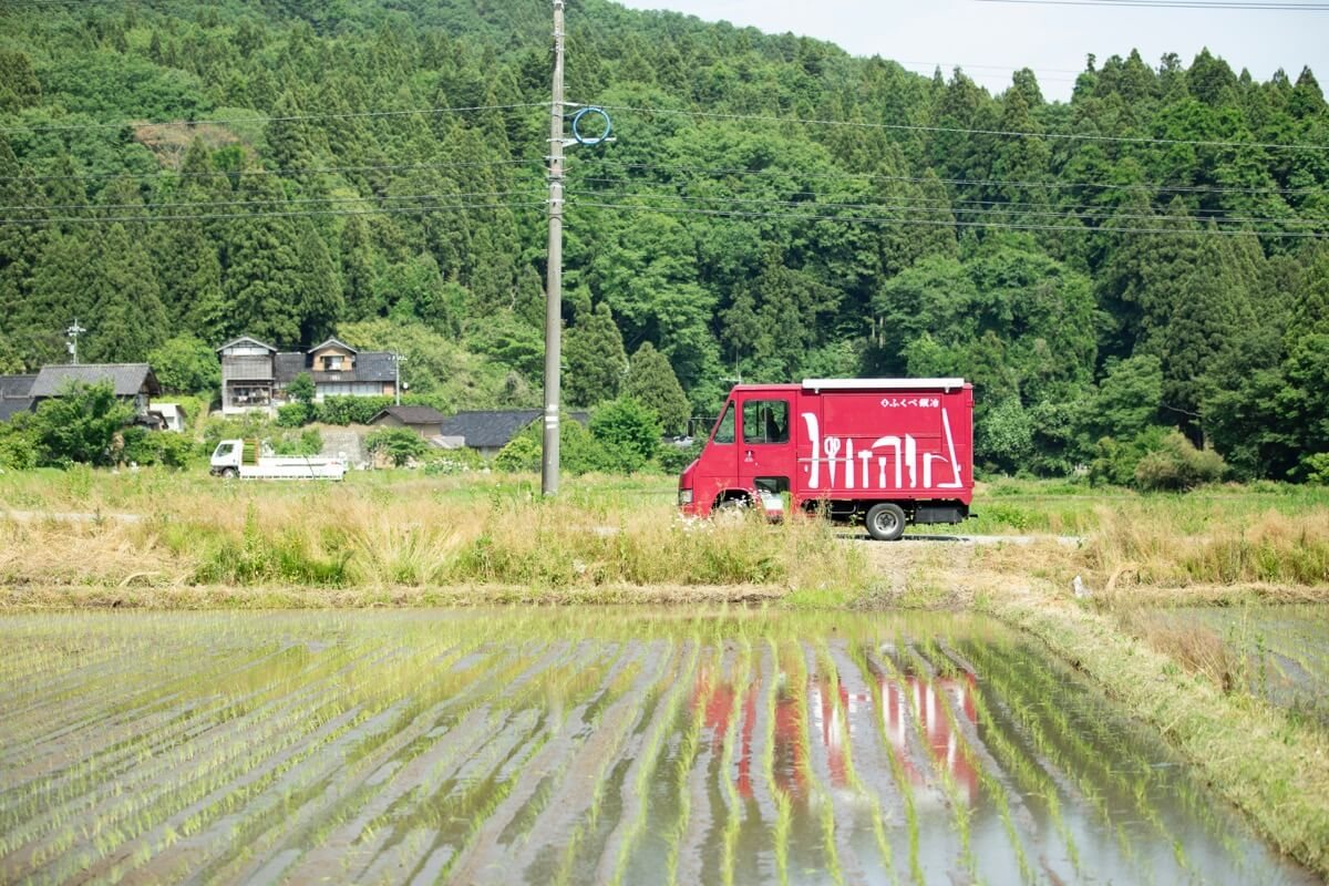 田んぼの向こうを走る赤い移動販売車