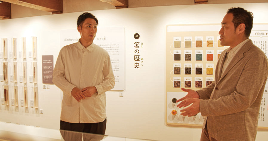 「箸の歴史」の展示パネルの前で話す二人